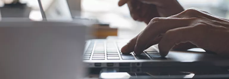 Close-up of hands typing on a laptop keyboard.