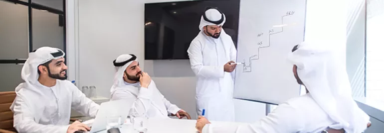 Business meeting with four men in white discussing a graph on a flip chart.