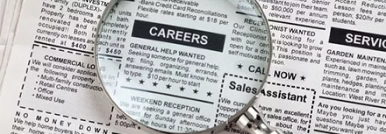 Magnifying glass over newspaper job ads section.