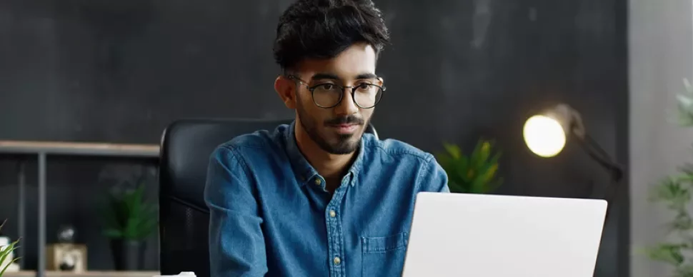 Man with glasses working on a laptop in a modern office.