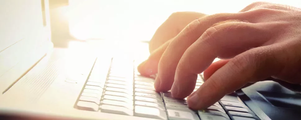 Hands typing on a laptop keyboard in bright light.