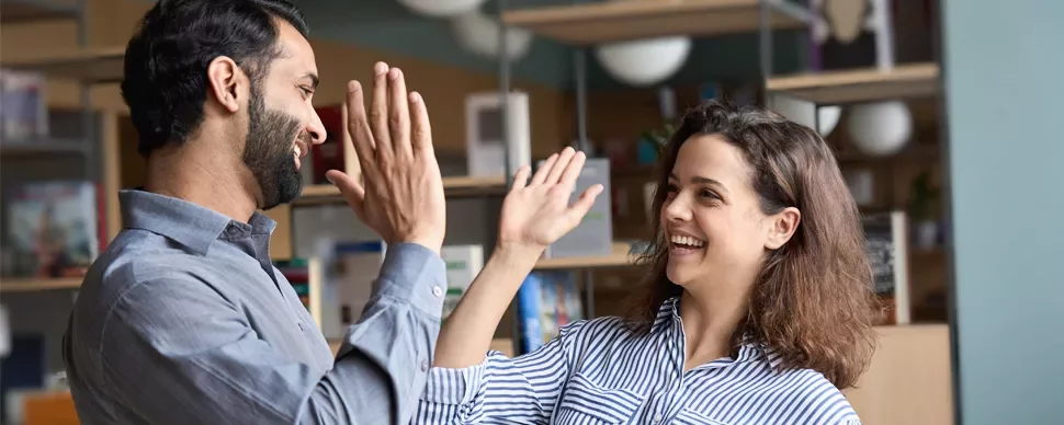 Two people smiling and giving high fives in a library setting.