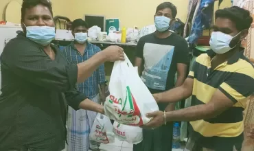 Group of people wearing masks handing out bags of supplies in a room.
