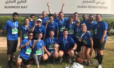 Group of marathon runners wearing blue shirts, holding medals at Business Bay in Dubai.