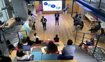 People in a modern meeting space with a presentation on screen.