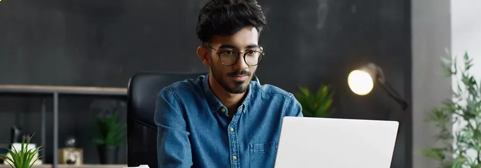 Man with glasses working on a laptop in a modern office.