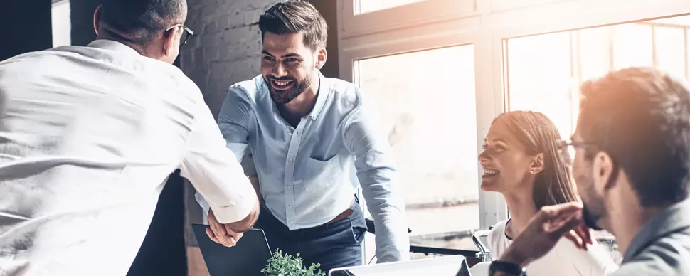 Group of professionals in a meeting, with a man shaking hands across the table.