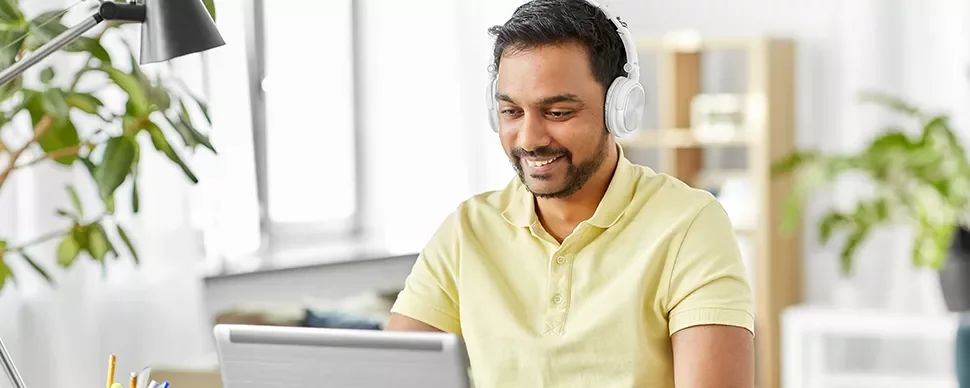 Man in yellow shirt wearing headphones, smiling while using a laptop.