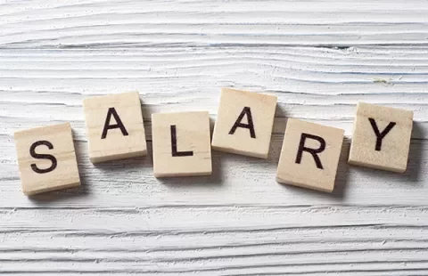 Wooden Scrabble tiles spelling 'SALARY' on a white wooden surface.