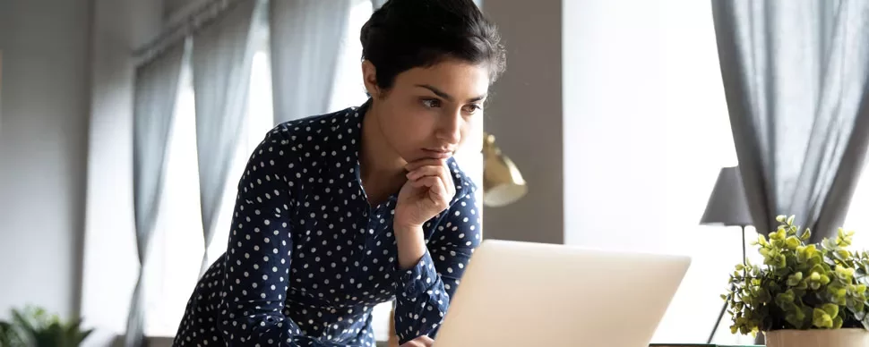 Woman in polka dot shirt working on a laptop at a desk.