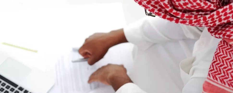 Person in a red keffiyeh signing a document at a desk.