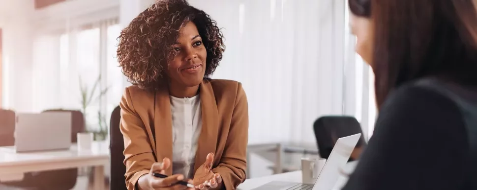 Two women having a friendly discussion in a modern office setting.