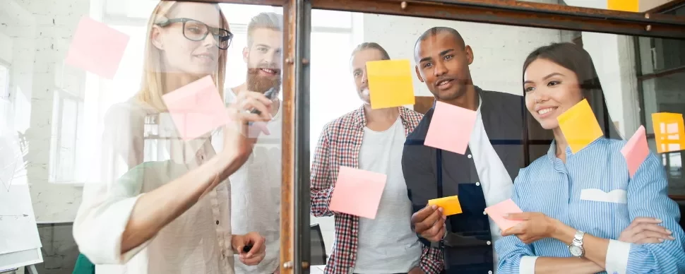 Group of colleagues brainstorming with sticky notes on glass board.