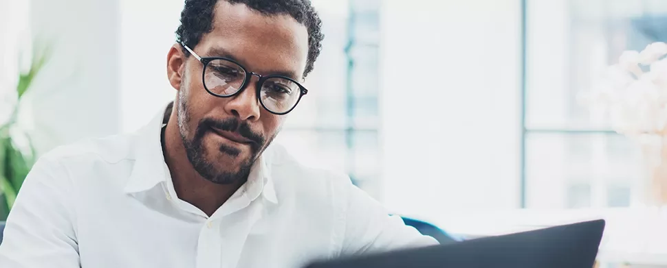 Man wearing glasses working on a laptop in a bright room.