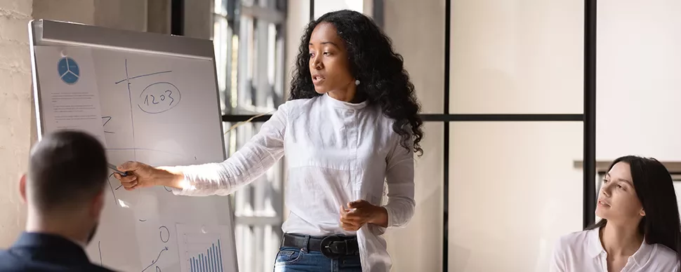 Woman presenting data on a flip chart to colleagues in a meeting room.