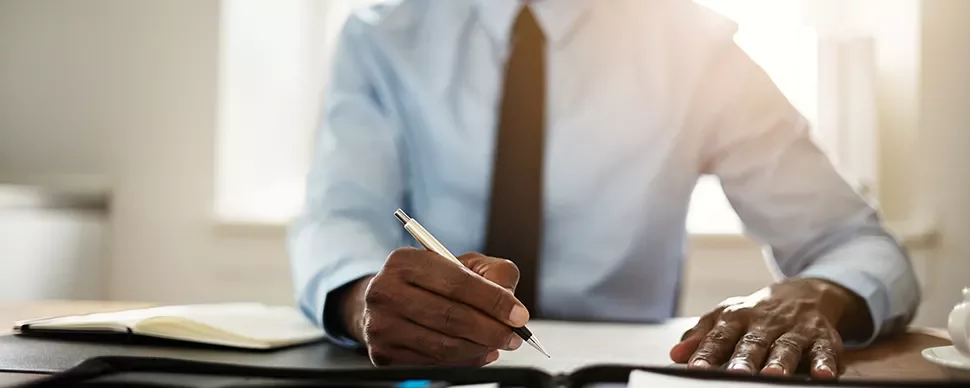 Person writing at a desk with notebook and pen.