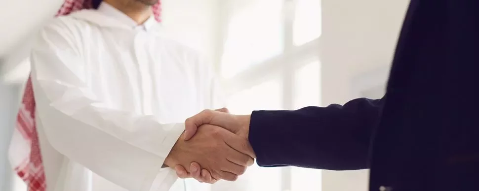Two people shaking hands, one in a white robe and others in a dark suit, symbolizing partnership.