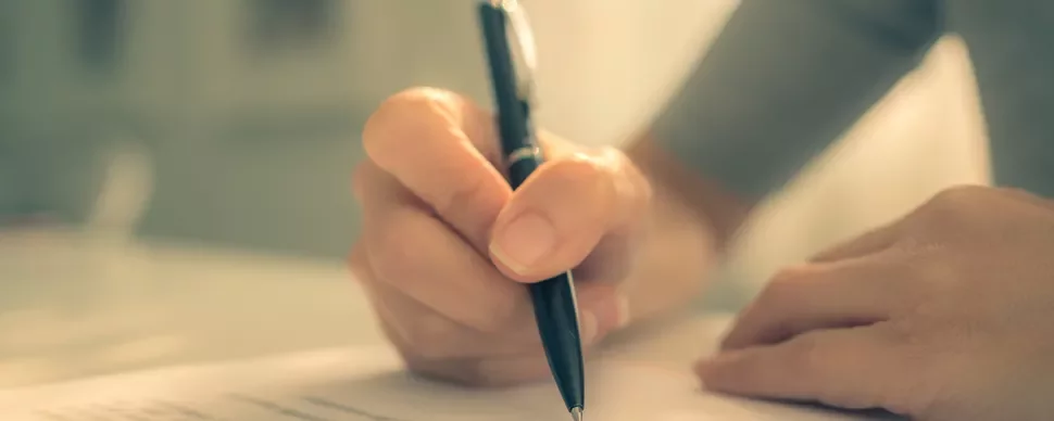 Close-up of a hand writing on paper with a pen.