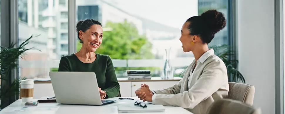 Two women engaged in discussion at a table with a laptop open between them