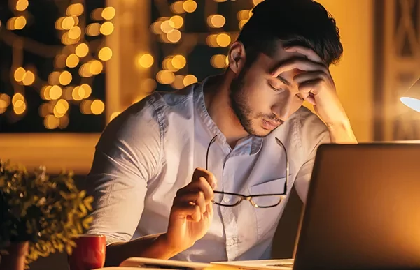 Man looking stressed while working on a laptop by night.
