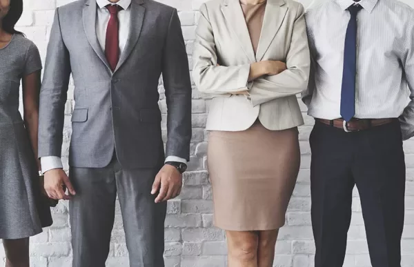 Business professionals in formal attire standing against a brick wall.