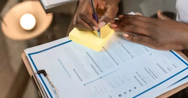 Person writing on sticky notes near a resume on a clipboard.