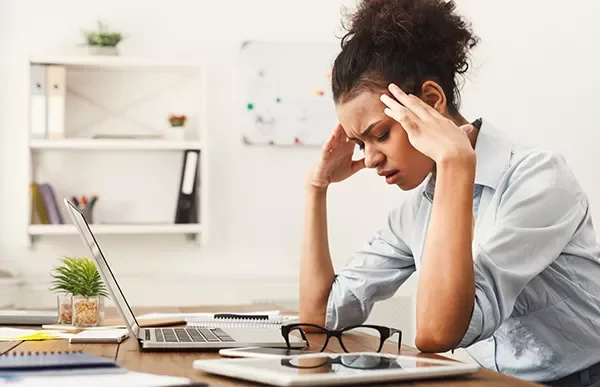 Woman sitting at a desk, looking stressed with her hands on her temples.