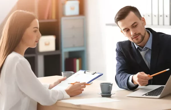 Two people discussing at a table with a laptop and clipboard.