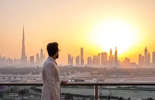 Man in white suit looking at Dubai skyline during sunset.