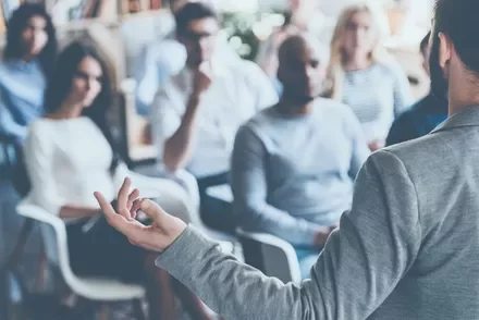 Person giving a presentation to a diverse group of people in a casual setting.