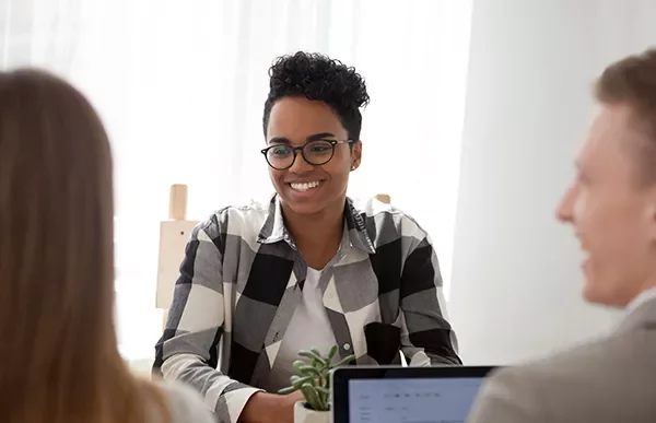 Smiling person in glasses at a desk during a meeting.