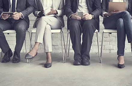 Row of business professionals seated, holding mobile devices and laptops.