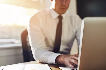 Man in white shirt and tie working on a laptop at a desk.