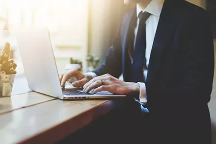 Businessperson typing on a laptop at a sunlit desk.