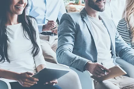 Smiling people sitting in a meeting taking notes.