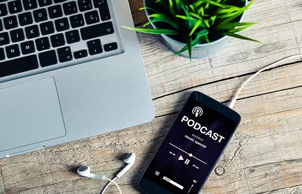 Smartphone on a wooden table playing a podcast beside a laptop and earphones.