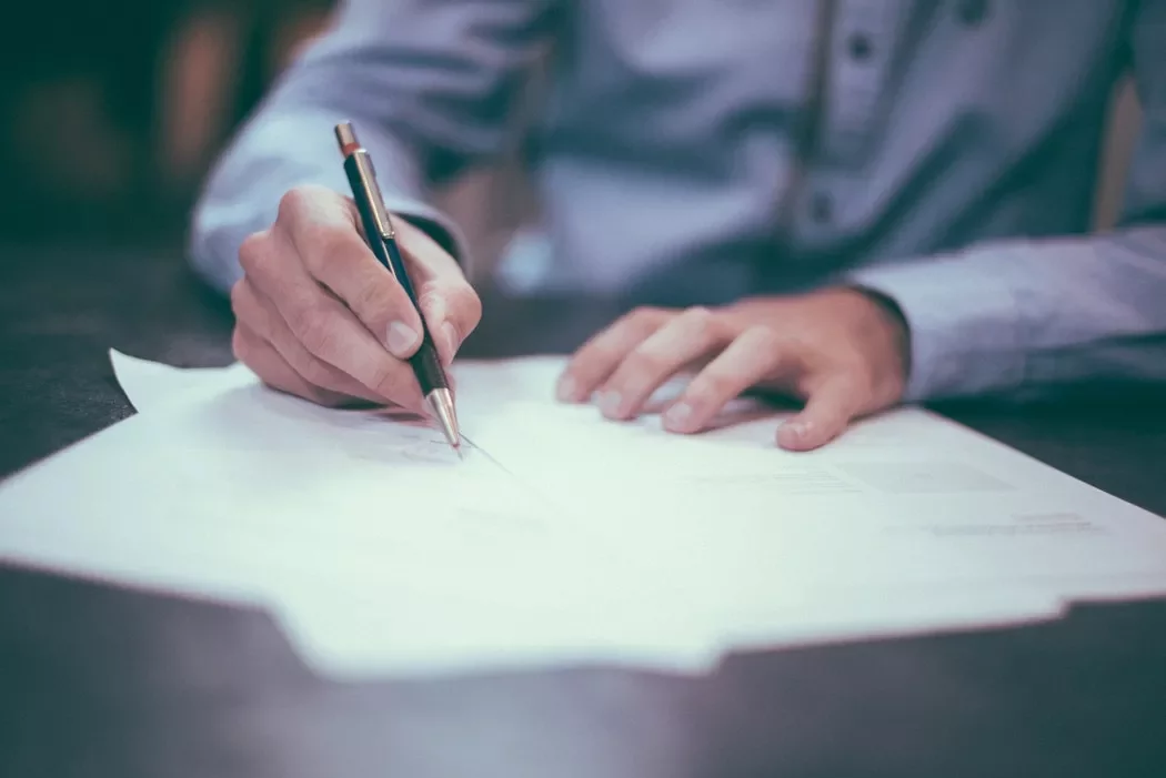 Person writing on white papers with a pen.