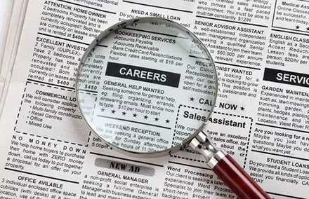 Magnifying glass over newspaper job ads section.