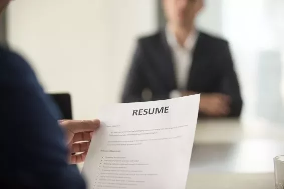 Person holding a resume during a job interview, facing a blurred figure in the background.