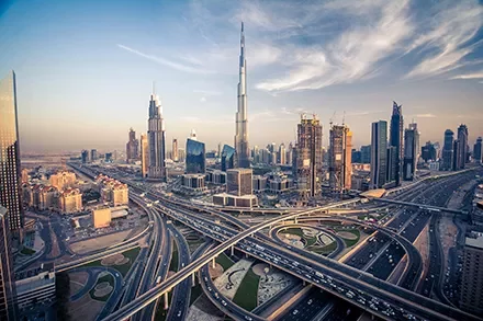 Aerial view of Dubai city skyline with modern skyscrapers and highways at sunset.